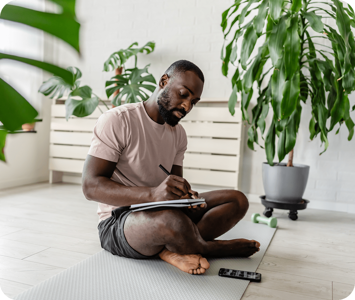 Man writing on notepad, sitting on floor.
